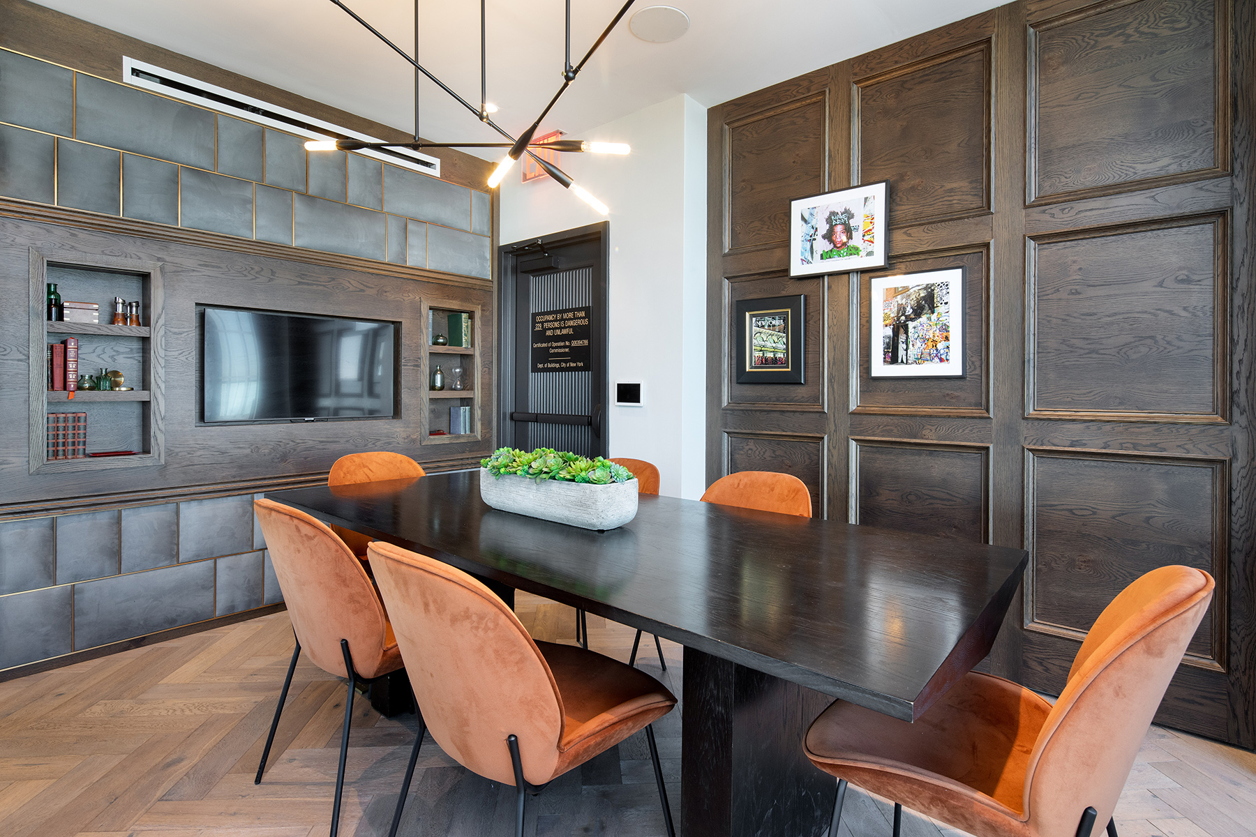 Private room with dark dining or conference table with contemporary chairs, built-in flat screen tv with shelving, modern lighting and wood floors
