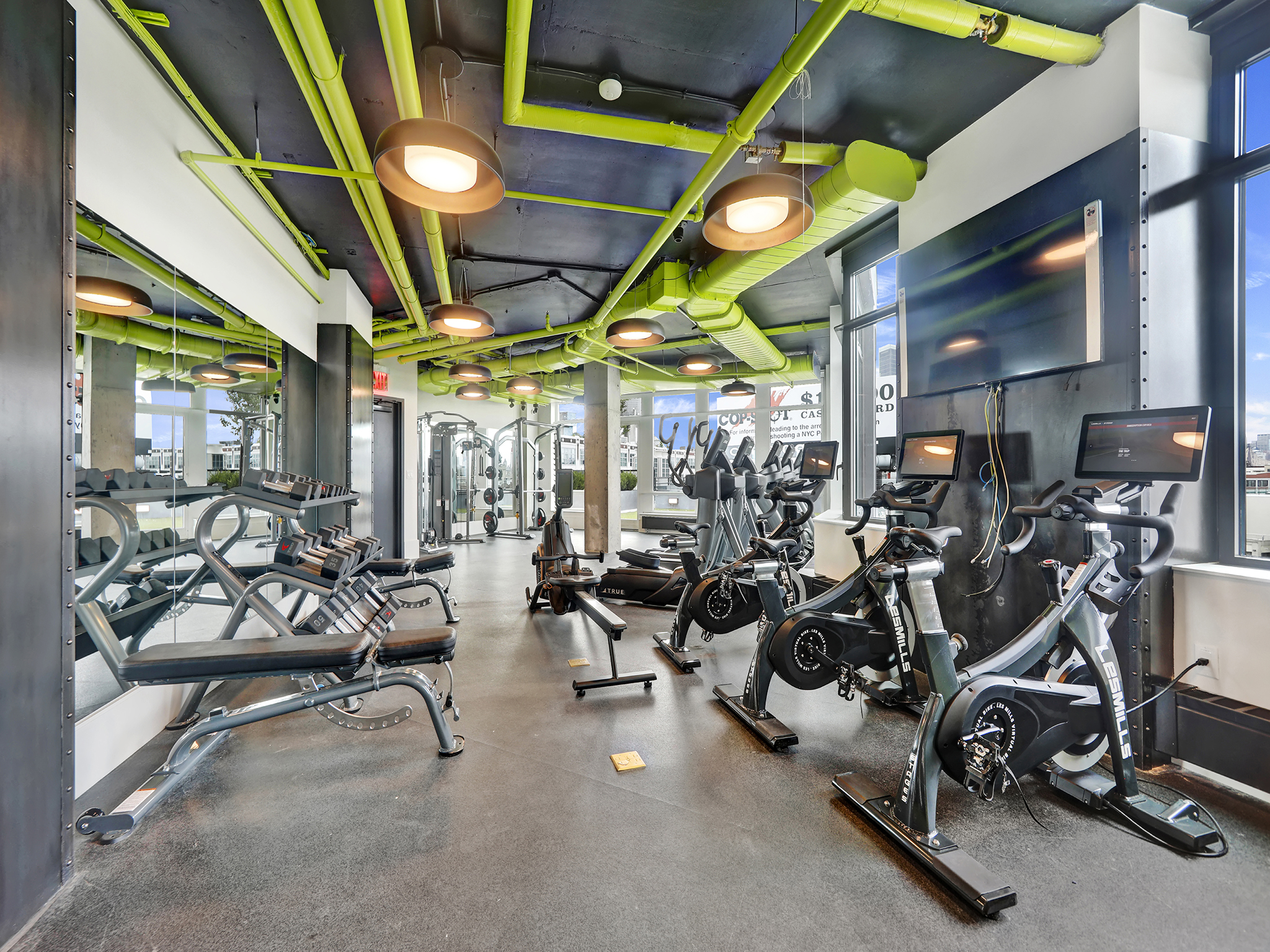 Bright fitness center with large windows, weights, ellipticals, bikes